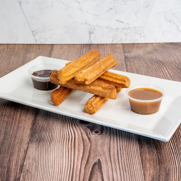 Don Eladio's Cantina churros, cinnamon-sugar coated, with chocolate and caramel dipping sauces on a white plate.
