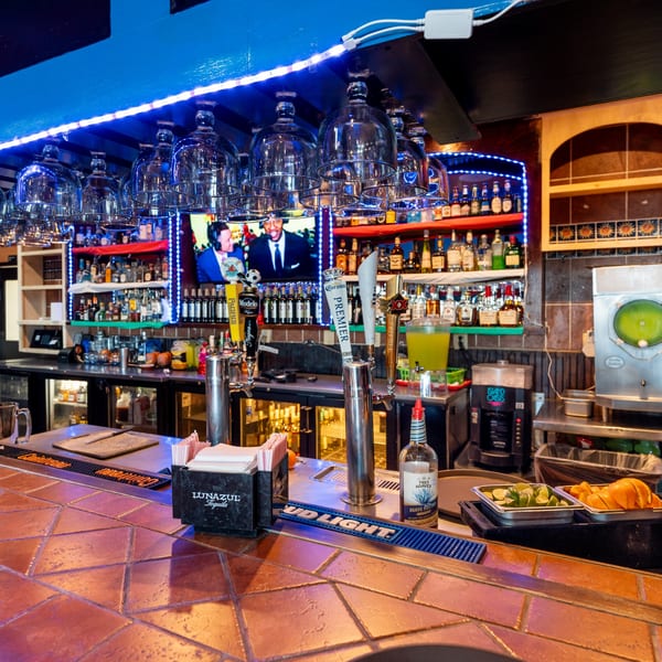 A vibrant bar at Don Eladio's Cantina with blue lighting, liquor bottles, beer taps, and a TV.