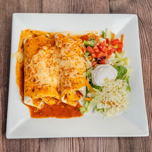 Two cheesy enchiladas covered in red sauce, served with a side salad and sour cream.