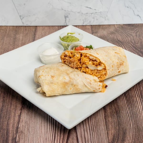 Two halves of a chicken and rice burrito with sides of guacamole, salsa, and sour cream.