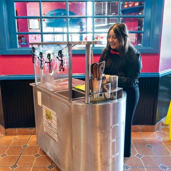 A smiling Don Eladio's Cantina employee stands by a stainless steel condiment station with skeleton decorations.