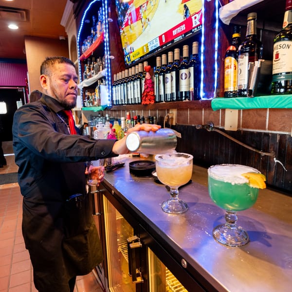Bartender at Don Eladio's Cantina pouring a margarita from a shaker, with two colorful drinks on the bar.