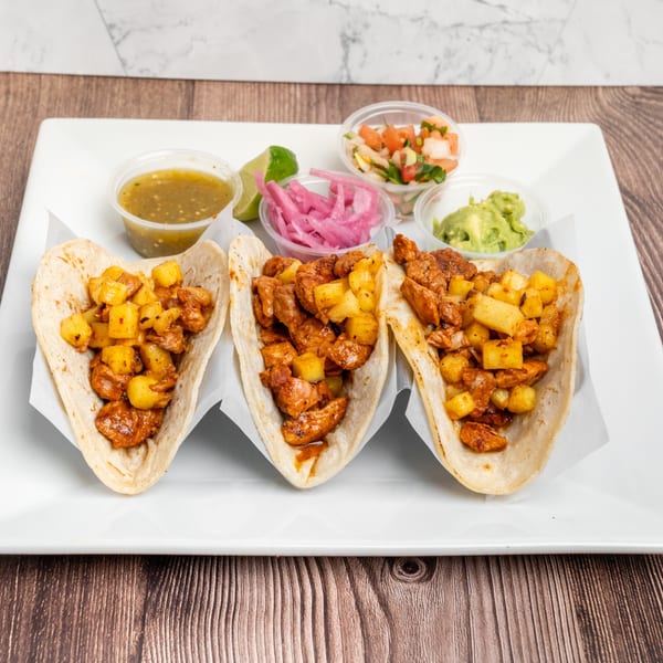 Three Don Eladio's Cantina tacos with meat and pineapple, served with salsa, guacamole, and pickled onions.