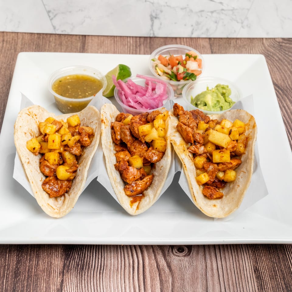 Three Don Eladio's Cantina tacos with meat and pineapple, served with salsa, guacamole, and pickled onions.